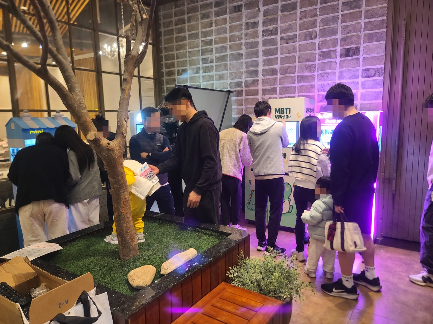 저녁 상가 거리 화단 옆에서 가족과 어린이가 MBTI 검사기에 참여하는 장면