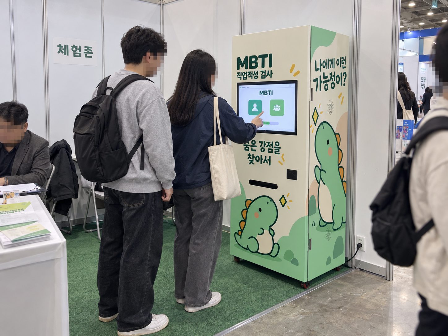 박람회 체험존 부스에서 대학생 두 명이 MBTI 검사기 화면을 보는 장면
